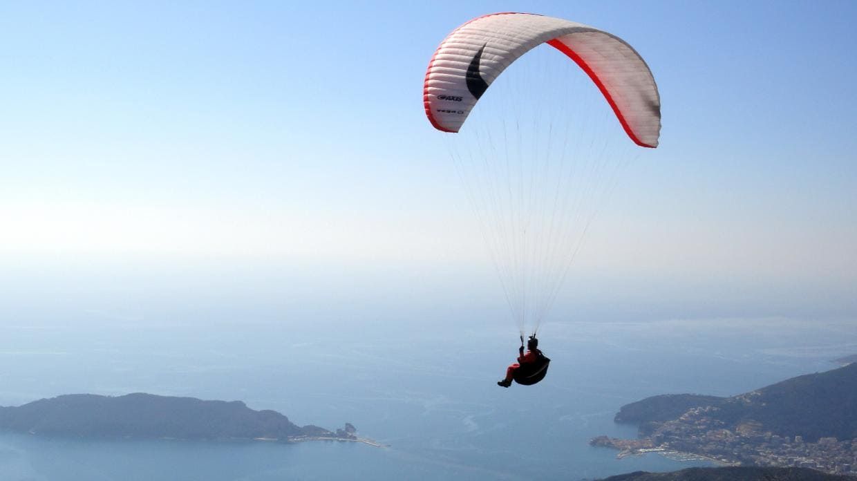 Paraglider flying above the Montenegro coast, used as the national paragliding guide image